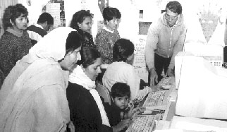 Photo of the group learning how to use a computer, while Azra's little son Mohammed looks on